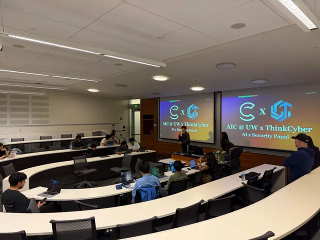 A speaker presenting to a full lecture hall, with two screens behind him displaying an "AIC @ UW x ThinkCyber — AI x Security Panel" title slide.