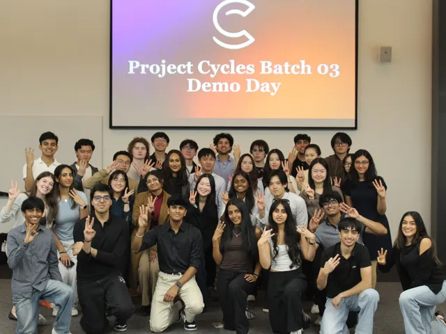 A large group of students posing together and holding up three fingers, in front of a screen reading "Project Cycles Batch 03 Demo Day."