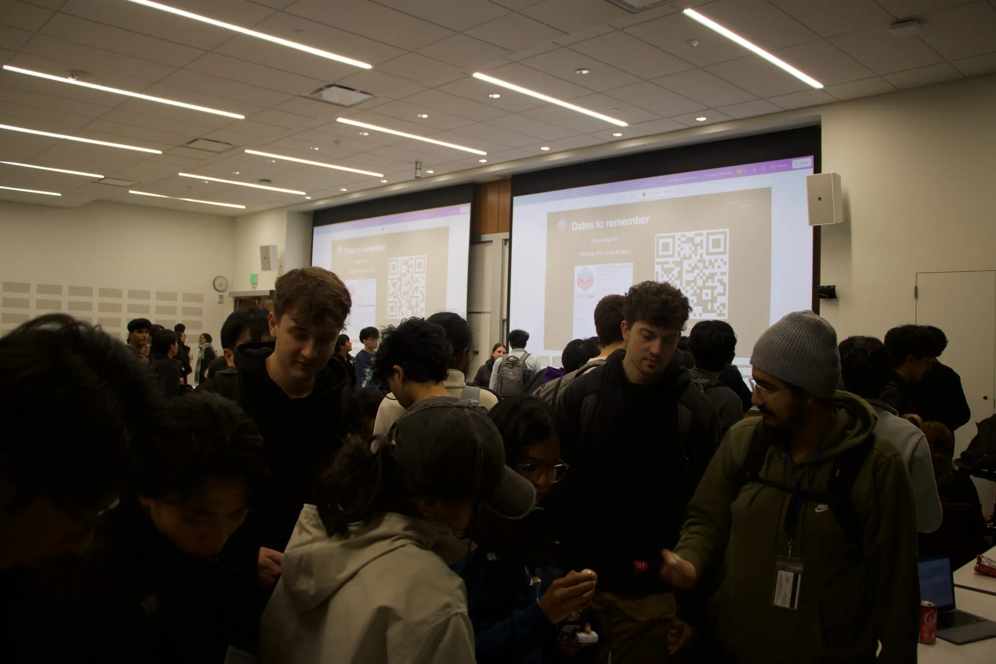 Students crowding a lecture hall after an event, in front of screens showing a slide titled "Dates to remember."