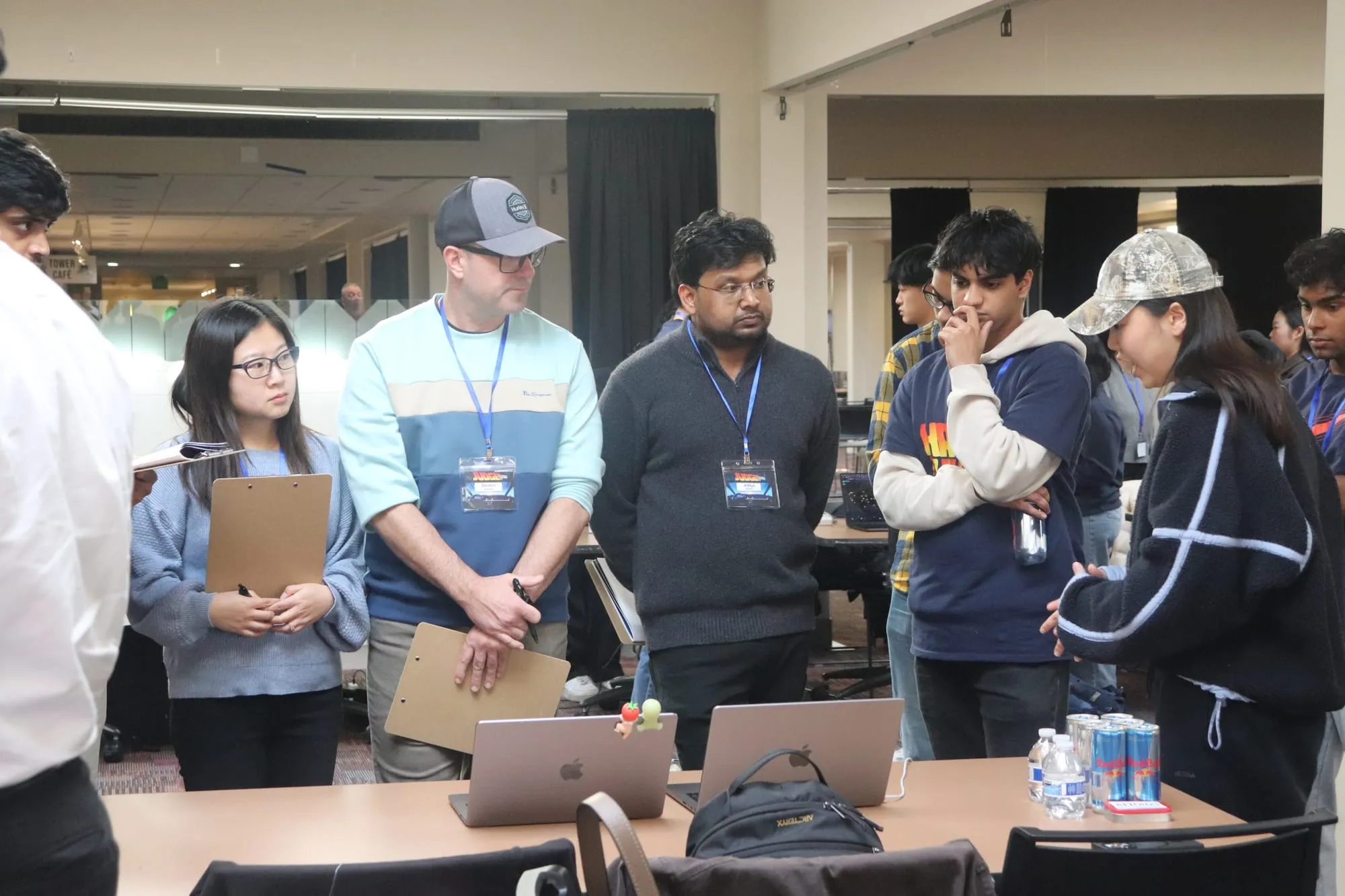 Judges with clipboards and name badges listening to a team at a table of open laptops.