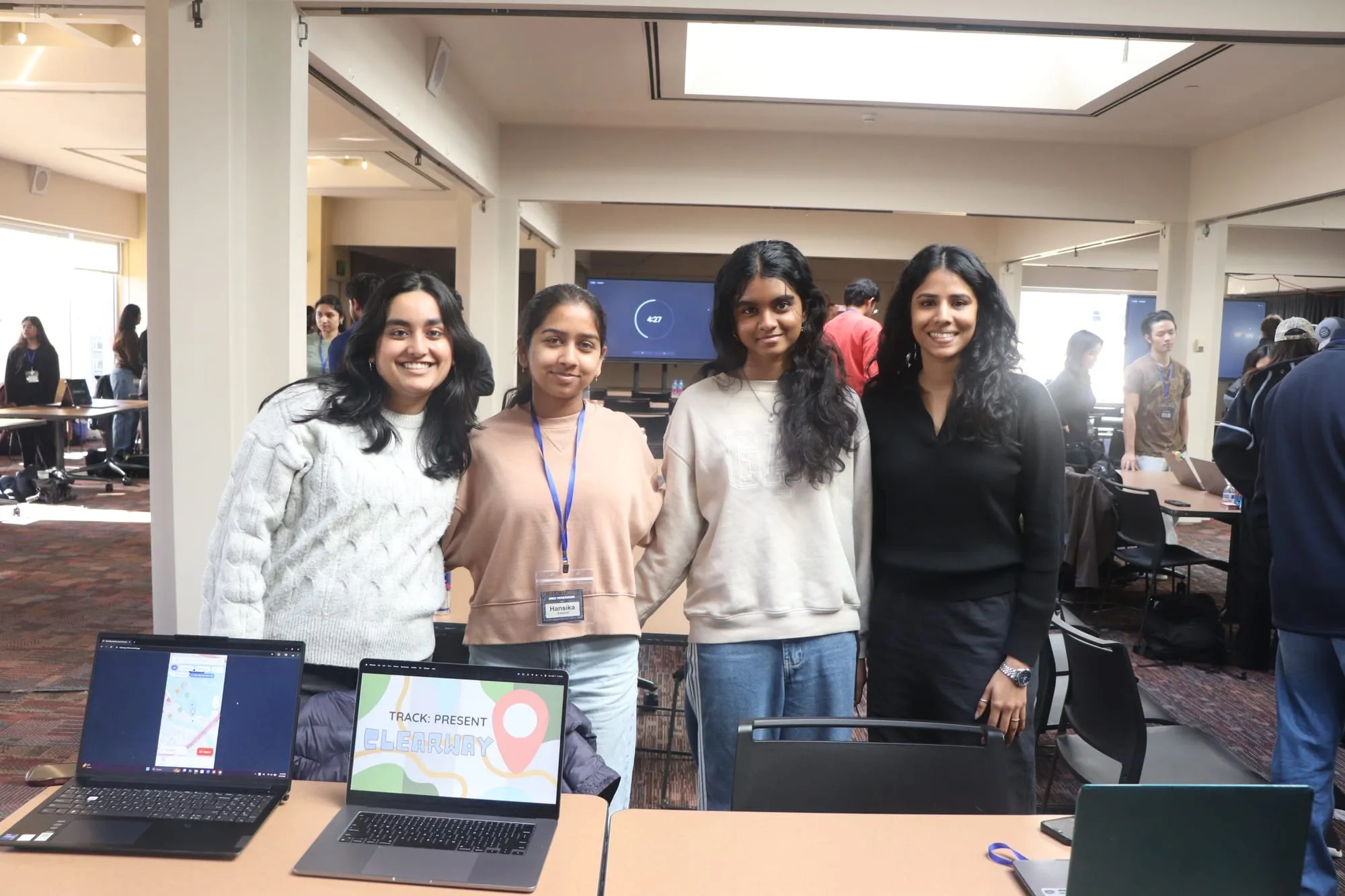 Four students standing behind a table with two laptops, one showing their project's title slide.