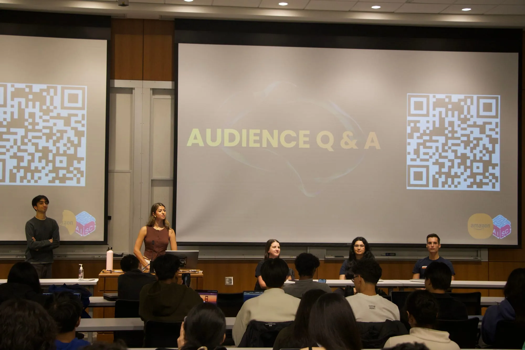 A panel at the front of a lecture hall, under a screen reading "Audience Q & A," facing a room of students.